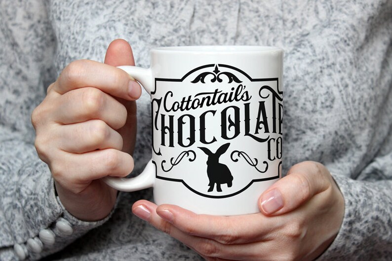 May include: White ceramic mug with a black and white logo that says "Cottontails' Chocolate Co." and features a silhouette of a rabbit.