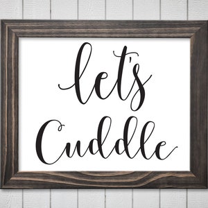 Könnte beinhalten: Ein schwarz-weißes Schild mit dem Text "Let's Cuddle" in einer kursivschriftlichen Schriftart. Das Schild ist in einem dunklen Holzrahmen gerahmt.