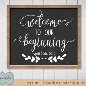 May include: A black chalkboard with a white wooden frame, featuring the text "welcomes to our beginning" in a cursive font. The date "April 20th, 2019" is written below the text, and a decorative branch with leaves is on either side of the date.