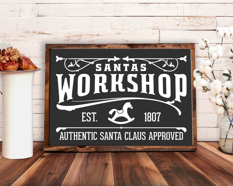 May include: Black and white sign with the text "Santa's Workshop" in a vintage style font. The sign also includes the text "Est. 1807" and "Authentic Santa Claus Approved".
