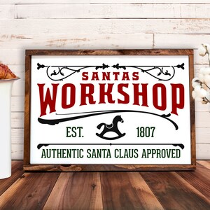 May include: A white sign with black and green text and a black rocking horse silhouette. The sign reads "Santa's Workshop Est. 1807 Authentic Santa Claus Approved".