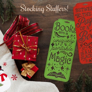May include: Two wooden bookmarks with festive Christmas-themed designs. The green bookmark reads "Books are a uniquely portable Magic" with a book and stars. The red bookmark reads "Between the Pages of a Book is a Lovely Place to Be".