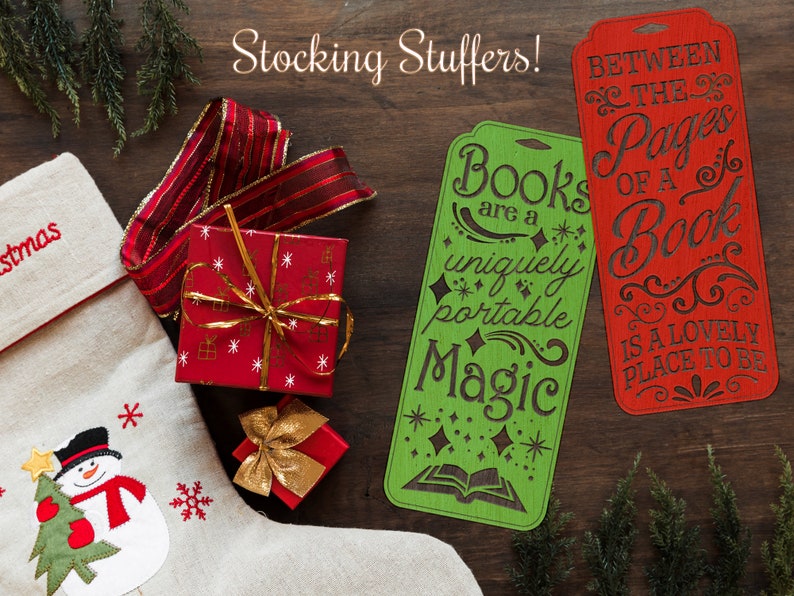 May include: Two wooden bookmarks with festive Christmas-themed designs. The green bookmark reads "Books are a uniquely portable Magic" with a book and stars. The red bookmark reads "Between the Pages of a Book is a Lovely Place to Be".