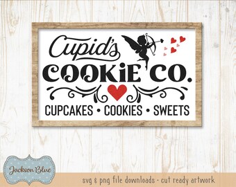 Op de afbeelding: Een wit bord met een bruin frame met de tekst "Cupid's Cookie Co." in zwart met een rood hart en een silhouet van Cupido die een pijl schiet. De tekst "Cupcakes Cookies Sweets" staat ook in zwart onder de hoofdtekst.