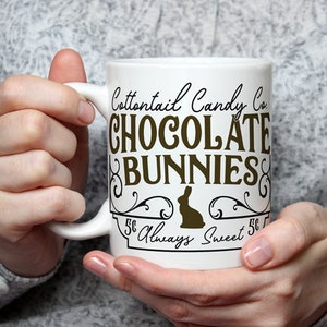 May include: White ceramic mug with a brown graphic that says "Cottontail Candy Co. Chocolate Bunnies 5&cent; Always Sweet 5&cent;". The graphic features a stylized bunny silhouette.