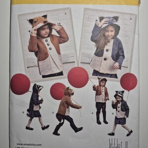 May include: Simplicity sewing pattern 1477A featuring children's costumes. The pattern includes designs for fox and raccoon hooded jackets with matching outfits. The image shows children wearing the costumes and holding red balloons. The size range is U.S. 3-8.