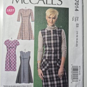 May include: McCall's sewing pattern M7014 featuring dress designs. The pattern includes a plaid dress, a patterned dress, and a houndstooth dress. The size is E5, fitting sizes 14-22. The word "EASY" is in a pink circle.