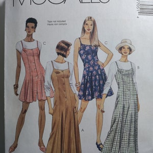 May include: A McCall's sewing pattern envelope featuring illustrations of four different dress and jumpsuit styles. The designs include a pink gingham dress, a solid tan jumpsuit, a blue floral dress, and a green gingham dress. Text reads Tops not included.