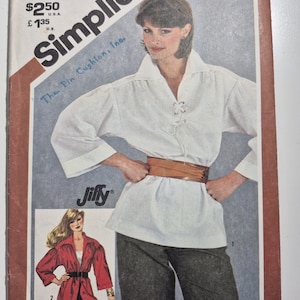 May include: A Simplicity 5479 sewing pattern envelope for a Jiffy top. The cover features a white long-sleeved shirt with a lace-up front and a brown waist belt, paired with dark trousers. A second illustration shows a red version of the top.