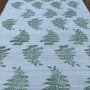 May include: A white table runner with a repeating pattern of green fern leaves.