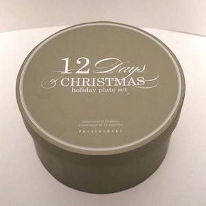 May include: A round, green box with a white label that reads "12 Days of Christmas holiday plate set". The box is made by Pottery Barn.