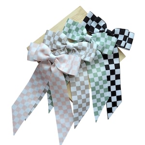 May include: Three checkered ribbon hair bows in pink, green, and black. The bows are tied in a large loop with two long tails.