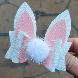 May include: A pink and white glitter bunny ear hair bow with a white pom-pom in the center.