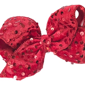May include: A large, red velvet hair bow adorned with numerous red sequins. The bow is tied in a classic style, with multiple loops and tails. The sequins add a touch of sparkle and texture to the accessory.