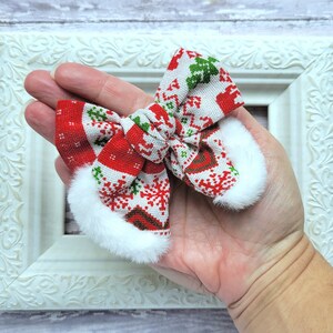 May include: A red and white Christmas-themed bow with a white faux fur trim. The bow is tied in a knot and has a snowflake pattern.