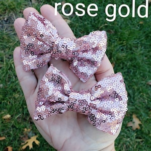 May include: Two rose gold sequined hair bows. The bows are tied in a classic bow shape and are made of small, shimmering sequins.