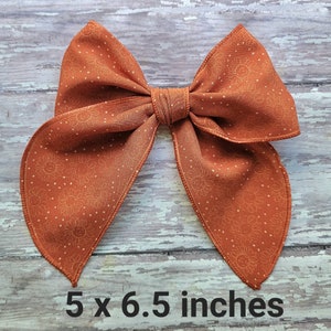 May include: A large orange bow with a white sun and dot pattern. The bow measures 5 x 6.5 inches.