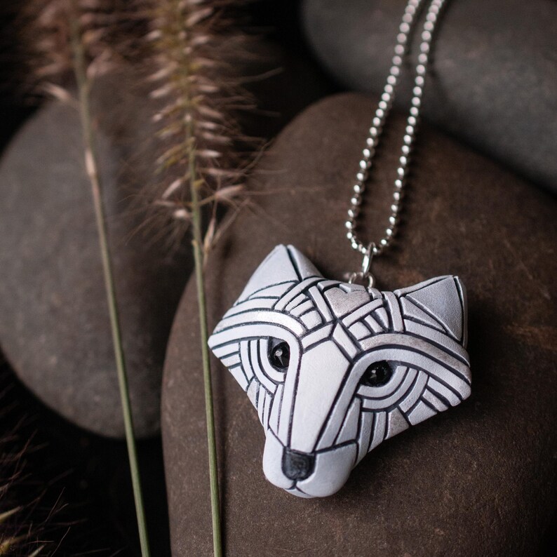 Photo shows a white Arctic fox necklace made in mosaic style from the front. Pendant hangs from a silver chain. Eyes are sparkling black crystals. Fits in the palm of your hand. Made to look like an ancient amulet.