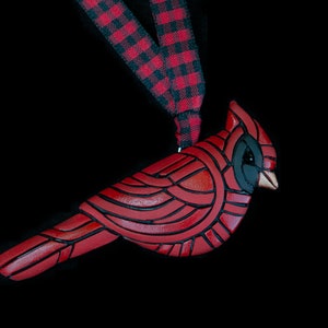 Photo shows a bright red cardinal ornament hanging from red and black plaid ribbons on black background.