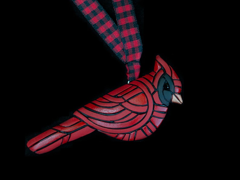 Photo shows a bright red cardinal ornament hanging from red and black plaid ribbons on black background.