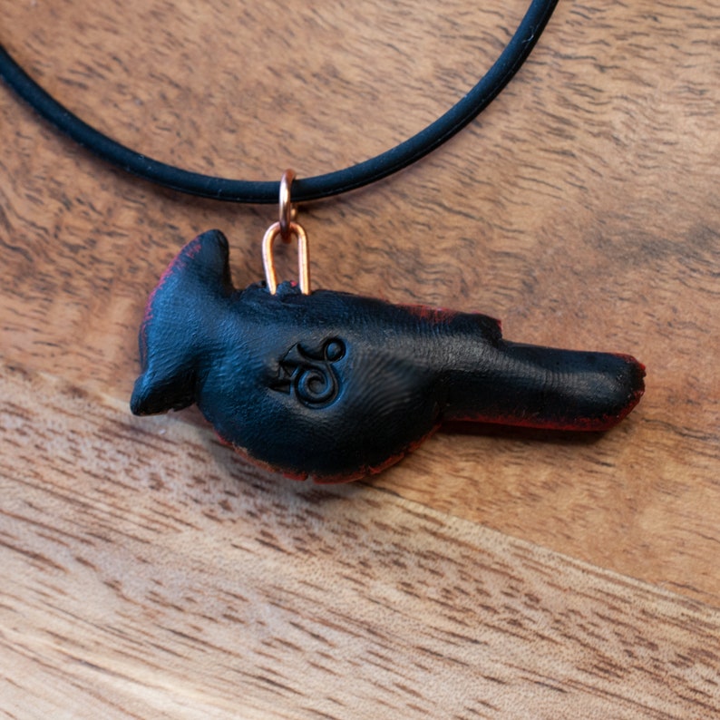 Photo shows the black back if the pendant. Maker's mark is stamped in the center.