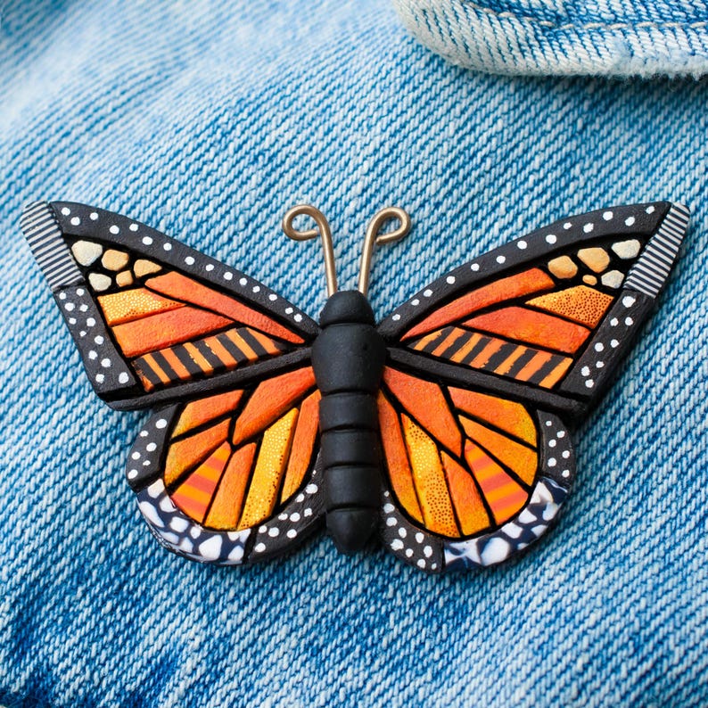 Bright Orange Monarch Butterfly pin on a denim jacket. Mosaic-style art brooch with bits of shine, texture and warm colors. Front angle