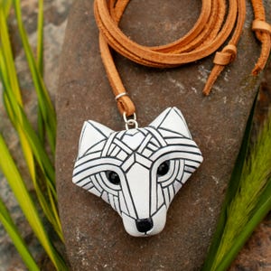 White Arctic fox necklace made in mosaic style is shown from the front. Pendant hangs from an adjustable tan leather cord. Eyes are sparkling black crystals. Fits in the palm of your hand. Made to look like an ancient amulet.
