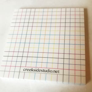 Może przedstawiać: Biały notes z siatką w kolorze czarnym, czerwonym, niebieskim, żółtym i jasnobrązowym. Na dole notesu znajduje się napis "creekside studio.net".