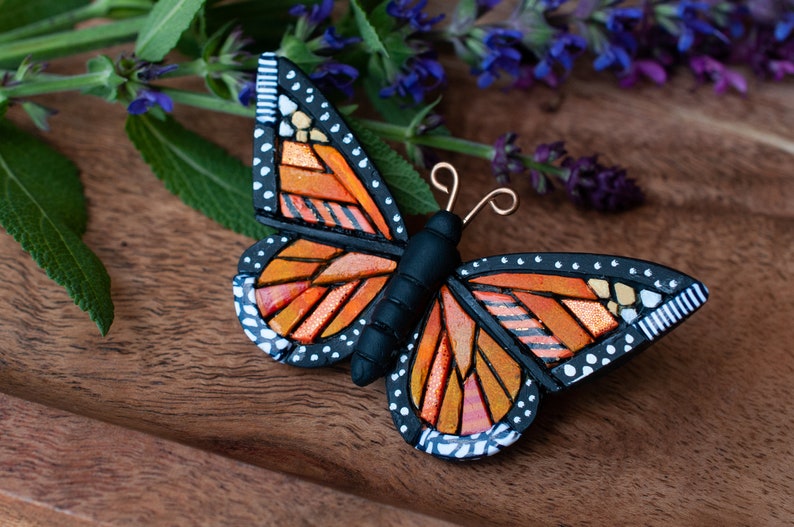 Orange Monarch Butterfly pin on a wooden tray. Mosaic-style art with bits of shine, texture and warm colors.
