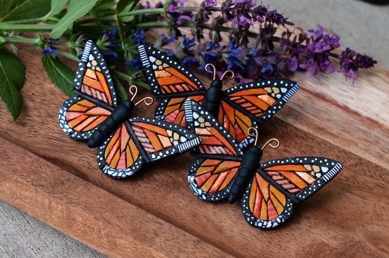 Group of 3 Bright Orange Monarch Butterfly pins on tray. Mosaic-style art brooches have bits of shine, texture and warm colors. Front angle