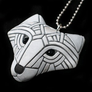 Photo shows a white Arctic fox necklace made in mosaic style from the side. Pendant hangs from a silver chain. Eyes are sparkling black crystals. Fits in the palm of your hand. Made to look like an ancient amulet.