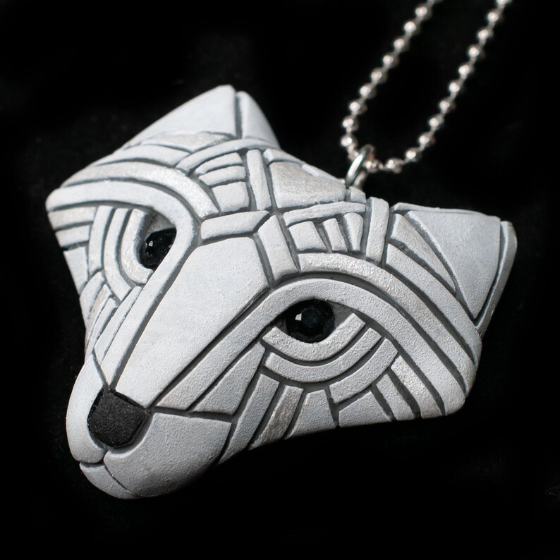 Photo shows a white Arctic fox necklace made in mosaic style from the side. Pendant hangs from a silver chain. Eyes are sparkling black crystals. Fits in the palm of your hand. Made to look like an ancient amulet.