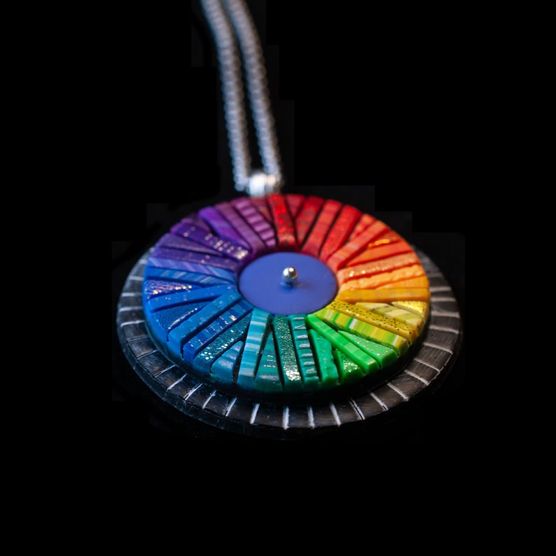 Photo shows mosaic rainbow fidget spinner in bright colors from the side. Spinner hangs from a silver chain.