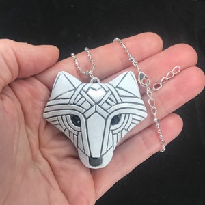 Photo shows a white Arctic fox necklace made in mosaic style from the front resting in a hand for scale. Pendant hangs from a silver chain. Eyes are sparkling black crystals. Fits in the palm of your hand. Made to look like an ancient amulet.