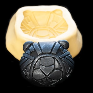 Peut inclure: Un moule en silicone pour réaliser un design de tête d'animal détaillé, géométrique, noir et gris. Le moule est jaune clair et a une surface lisse. Le moule est présenté avec un produit fini, une tête d'animal noire et grise.