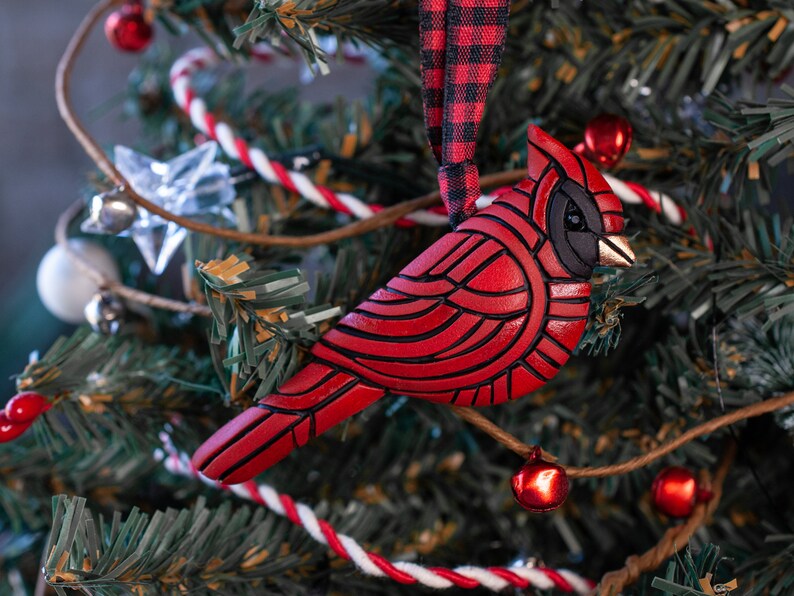Photo shows bright red cardinal mosaic ornament on a red plaid ribbon hanging on a Christmas tree.