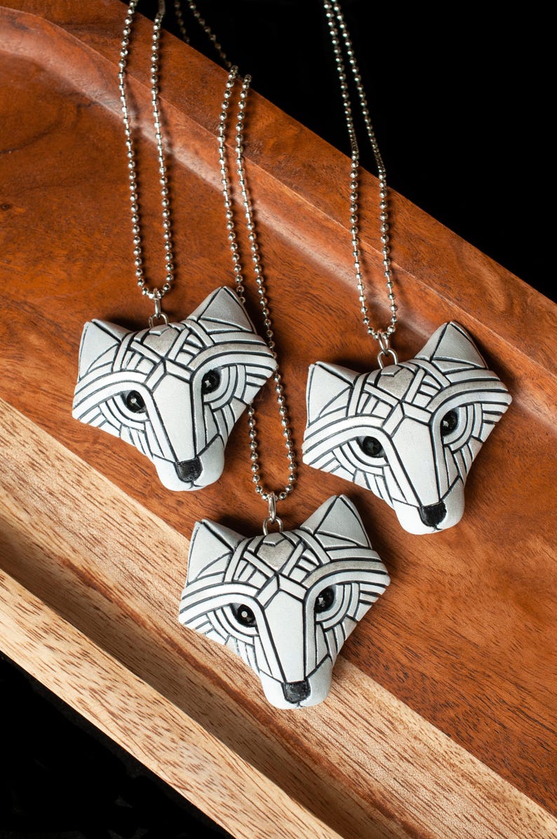 Photo shows group of three white Arctic fox necklaces made in mosaic style from the front view. Pendants hang from silver ball chains. Eyes are sparkling black crystals. Fits in the palm of your hand. Made to look like an ancient amulets.