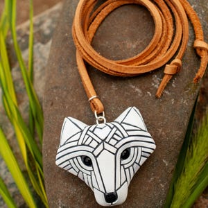 White Arctic fox necklace made in mosaic style is shown from the front. Pendant hangs from an adjustable tan leather cord. Eyes are sparkling black crystals. Fits in the palm of your hand. Made to look like an ancient amulet.
