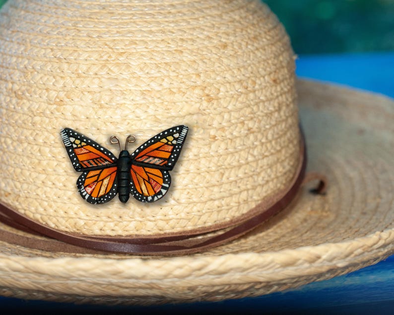 Bright Orange Monarch Butterfly pin on summer hat. Mosaic-style art brooch with bits of shine, texture and warm colors. Front angle