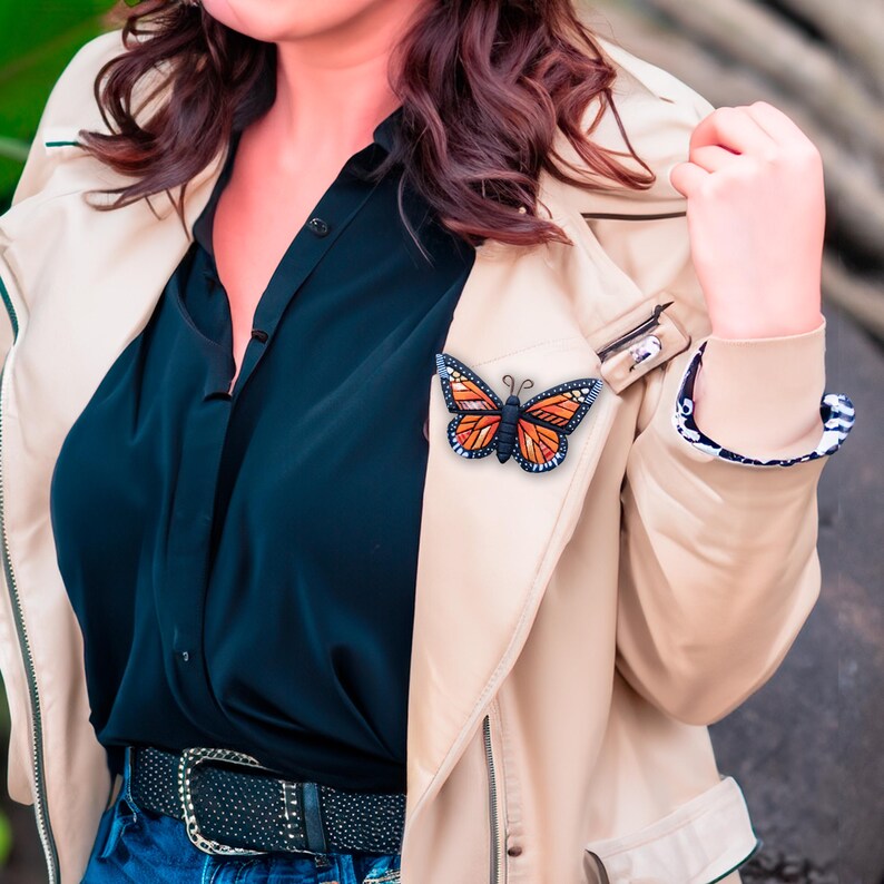 Bright Orange Monarch Butterfly pin on model. Mosaic-style art brooch with bits of shine, texture and warm colors. Front angle