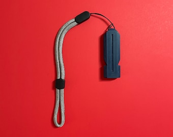 Op de afbeelding: Een marineblauwe, rechthoekige USB-stick met een grijze polsband en zwarte connectoren. De polsband is gemaakt van een geweven, grijs materiaal. De achtergrond is effen rood.