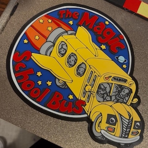 Op de afbeelding: Een gele schoolbus met een raketbooster, met de tekst "The Magic School Bus" in het rood. De bus heeft passagiers zichtbaar in de ramen en staat tegen een blauwe achtergrond met sterren en een planeet.