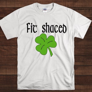 May include: White t-shirt with the text "Fit shaced" and a green four-leaf clover.