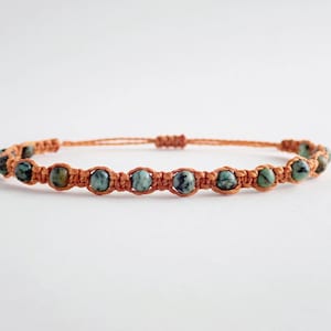May include: A brown cord bracelet with green and black patterned beads.