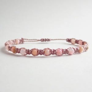 May include: A pink gemstone bracelet with pink cord and a knotted closure.