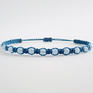 Puede incluir: Un brazalete de macramé azul con cuentas de color azul claro.