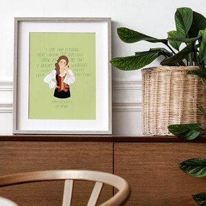 May include: Framed art print featuring a cartoon illustration of Fran Drescher from The Nanny, with a quote from the show. The artwork has a light green background and is in a gray frame. The print is displayed on a wooden cabinet.