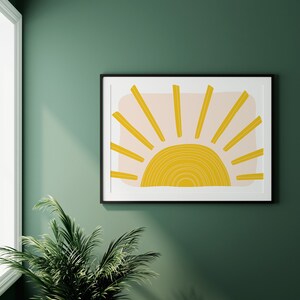 May include: A framed print of a stylised sun with yellow and peach colours on a green wall.