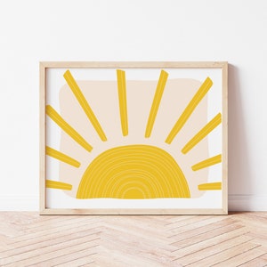 May include: A framed print of a minimalist sun design with a yellow sun and rays on a light pink background.