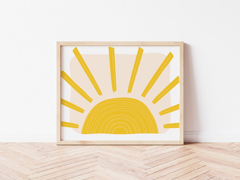 May include: A framed print of a minimalist sun design with a yellow sun and rays on a light pink background.